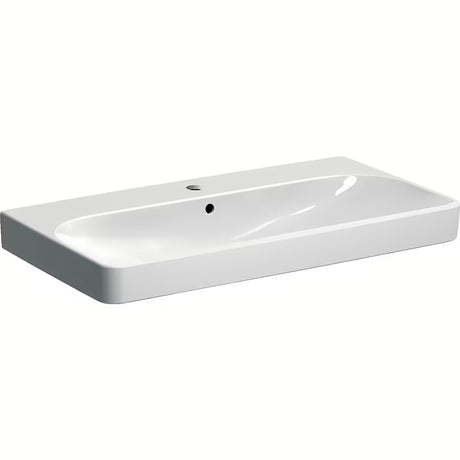 Bílé závěsné umyvadlo Geberit Smyle Square 90x48 cm ze sanitární keramiky s přepadem a otvorem pro baterii.