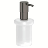 Dávkovač mýdla Grohe Essentials bez držáku v provedení hard graphite, skleněná nádobka a kovové prvky.